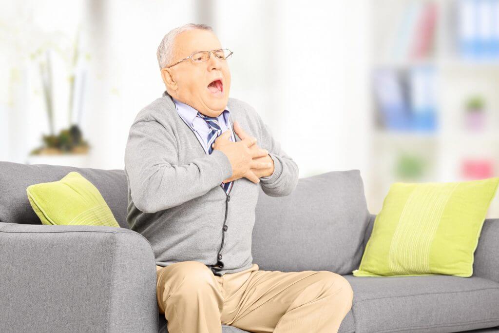 Senior man seated on a sofa having a heart attack at home